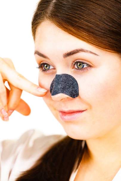 Woman appying clear-up strips on nose, using pore cleansing textile mask, on white. Girl taking care of skin complexion. Beauty treatment. Skincare. - Photo, image