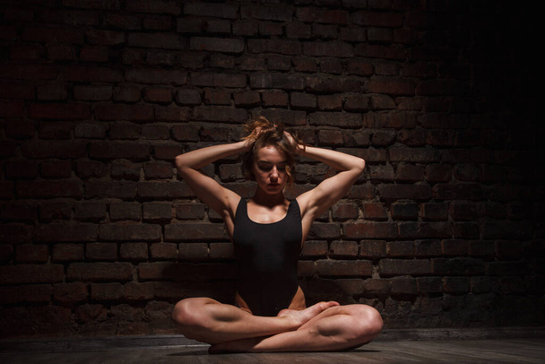 Meisje in zwart badpak doet yoga tegen de achtergrond van een bakstenen muur - Foto, afbeelding
