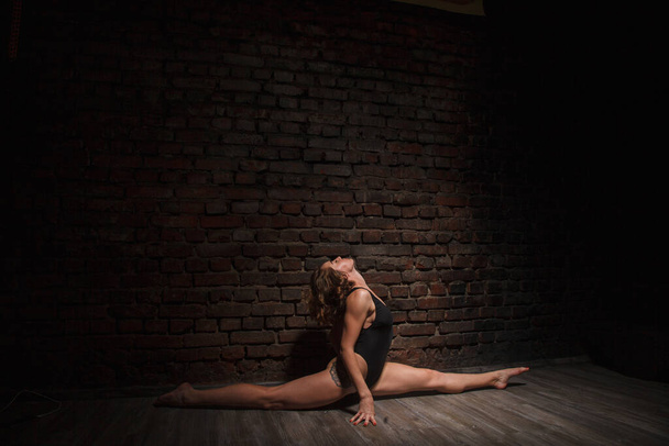 Chica en traje de baño negro hace yoga contra el fondo de una pared de ladrillo
 - Foto, imagen
