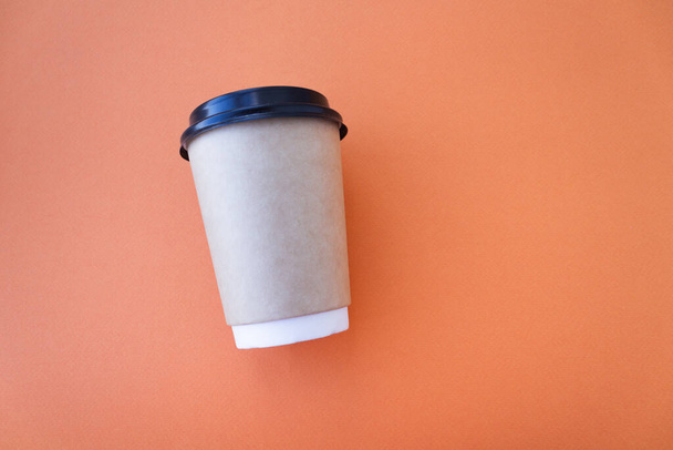 Coffee to go concept. Disposable craft cup with black plastic cover on a trendy orange background. Place for text. Flat lay style. Top view - Zdjęcie, obraz