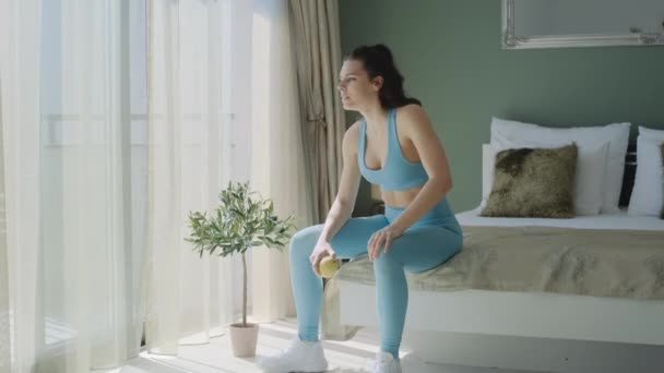 Fitness millennial woman in blue casual clothes eating an apple after sport  workout at home. Tired athletic lady resting after exercise on the body. - Filmagem, Vídeo