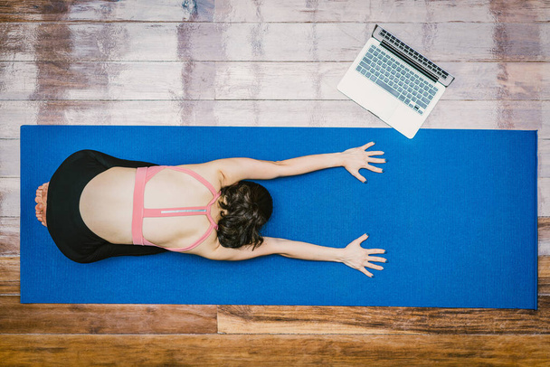 Asiatin praktiziert Yoga von zu Hause aus mit Laptop bei Covid19-Ausbruch, gesunde oder Meditationsübungen, Training zu Hause, Coronavirus-Pandemie und Quarantäne, Sport und Gesundheitsfürsorge im Konzept - Foto, Bild