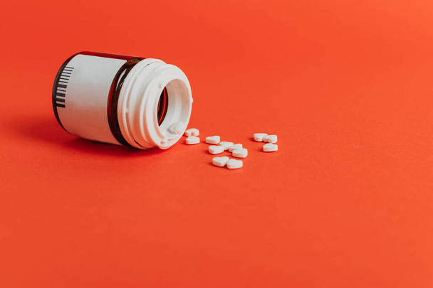 Vérnyomás, szívbetegségek gyógyszerei. Kis fehér szív alakú tabletták és üveg piros színes háttér. - Fotó, kép