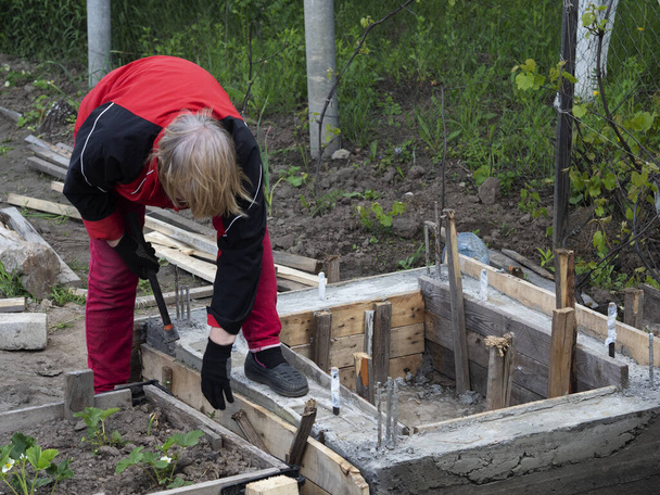 Senior Caucasian woman removes formwork from a strip foundation in a garden - Фото, зображення