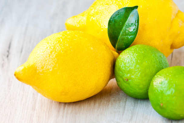 Closeup of juicy bright citrus fruits on a table in the bright rays of the morning light - lemons and lime with a green leaf - Foto, Imagen