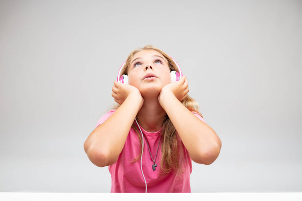 Chica joven inmersa en escuchar su música en un par de auriculares rosados mirando hacia arriba con una expresión absorbida sobre blanco
 - Foto, imagen