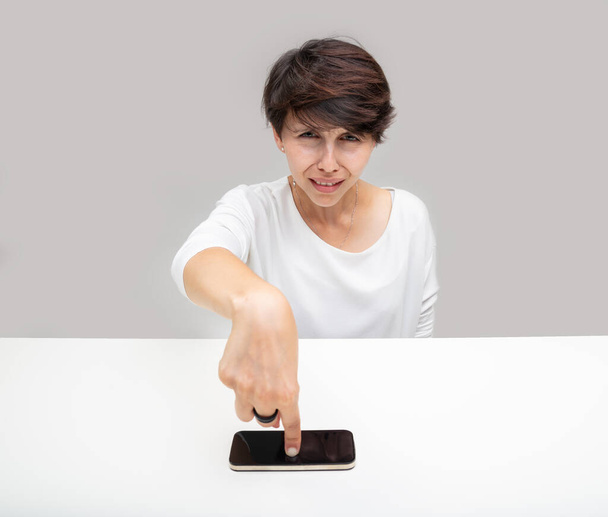 Mujer intensa apuntando a su teléfono móvil con un fruncido desconcertado mientras presenta pruebas en una discusión o conversación
 - Foto, imagen