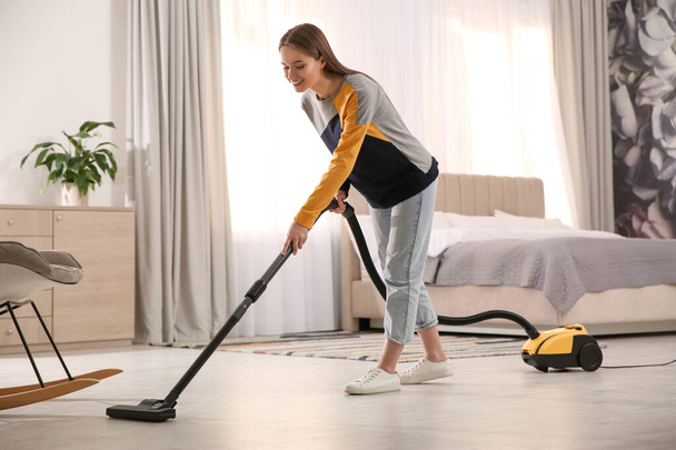 Young woman using vacuum cleaner at home - Fotografie, Obrázek