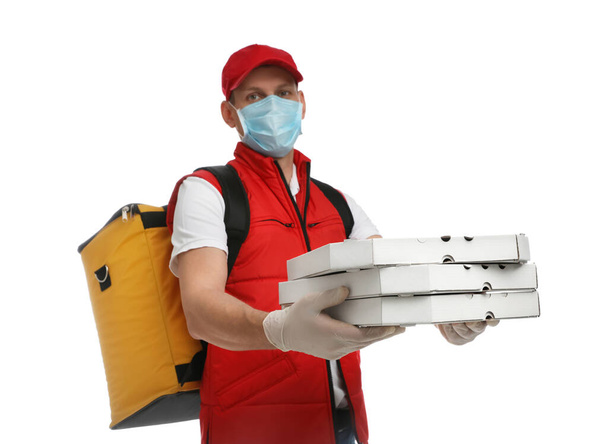 Courier in protective mask and gloves holding pizza boxes on white background. Food delivery service during coronavirus quarantine - 写真・画像
