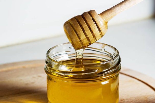 Honey with a wooden honey ladle drips on a wooden table - 写真・画像