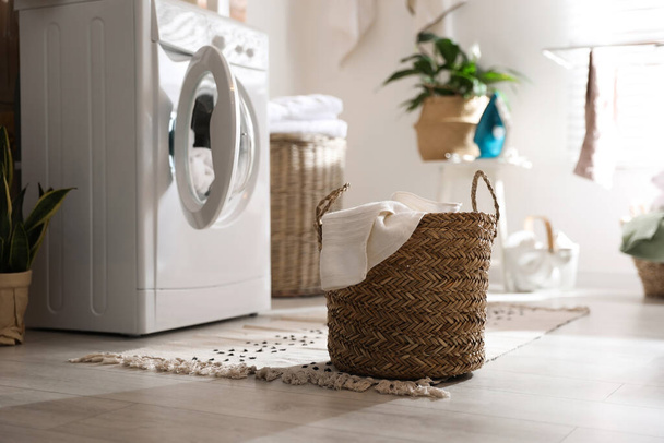 Wicker basket with laundry near washing machine indoors. Interior element - Valokuva, kuva