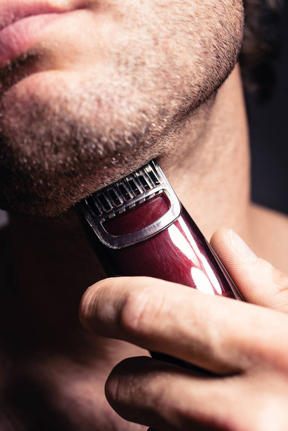 A man shaves his face with an electric razor - Фото, изображение