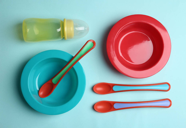 Set of colorful plastic dishware on light blue background, flat lay. Serving baby food - Foto, afbeelding