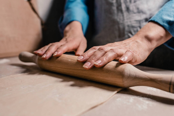 A baker hands with a wooden rolling pin rolls the dough into a thin layer on the table - Foto, immagini
