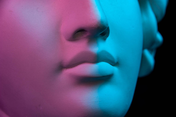 Colorful gypsum copy of ancient statue of human head for artists on a black background. Close up view lips. Plaster sculpture of human face. Toned blue and purple. Webpunk, surreal style poster. - Фото, изображение