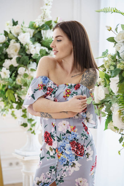 Beautiful brunette woman in colorful summer dress posing next to white flowers at luxury apartments  - Foto, Imagen