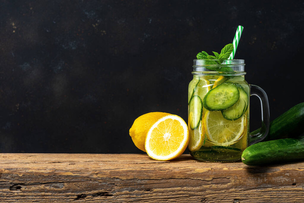 Detox water with sliced lemon and cucumber in a jar on dark background. Healthy concept. - Foto, Imagem