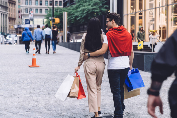 From behind trendy modern casual loving young man and woman with shopping bags walking along city street  in daylight - Fotoğraf, Görsel
