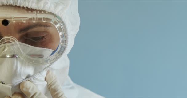 Doctor in protective suit with face mask, eyeglasses and gloves portrait. Nurse in protective suit with face mask, eyeglasses and gloves. Woman wearing protection suite. Copyspace - Filmati, video