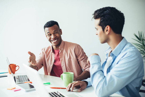 Glückliche männliche Programmierer diskutieren Start-up mit der Erstellung von Webseiten am Schreibtisch und lächeln, qualifizierte Mitarbeiter genießen Teamarbeit und Brainstorming auf Online-Service-Plattform für Millennials - Foto, Bild