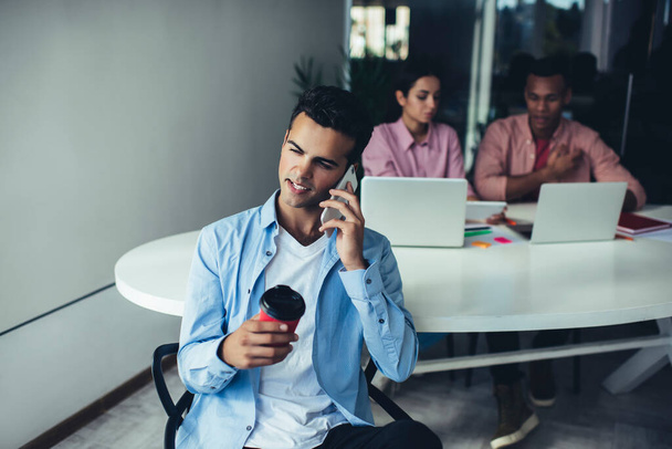 Young Spanish executive manager with coffee to go using 4g wireless for making online mobile cell call, millennial employee talking with colleague during smartphone conversation via application - Foto, Imagem