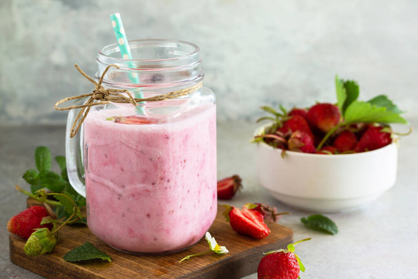 Natural detox, fruit dessert, healthy dieting concept. Strawberry fruit Yogurt smoothie or milk shake in glass jar on a light stone or slate table. - 写真・画像