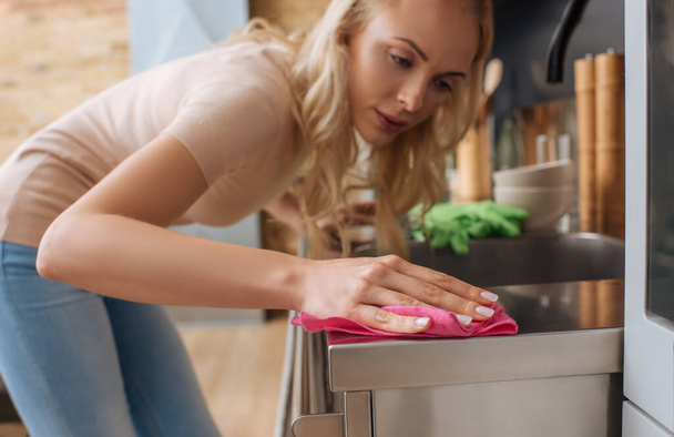 selective focus of young housewife cleaning surface of kitchen furniture with rag - Photo, Image