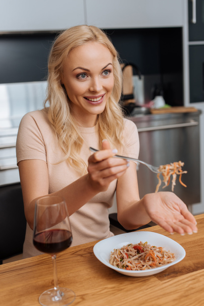 赤いワインのグラスの近くにタイの麺とフォークを持った笑顔の女性 - 写真・画像