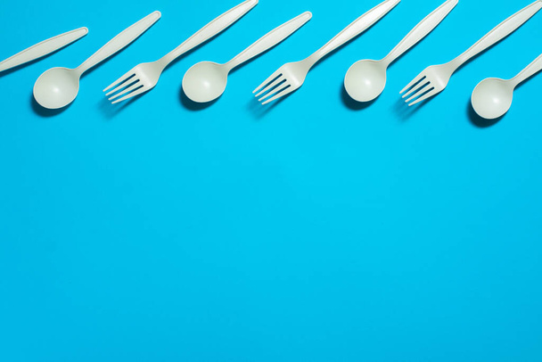 eco-friendly disposable tableware on a blue background. isolate. corn starch spoons and forks. biodegradable dishes. natural materials for replacing plastic. place for text - Foto, imagen