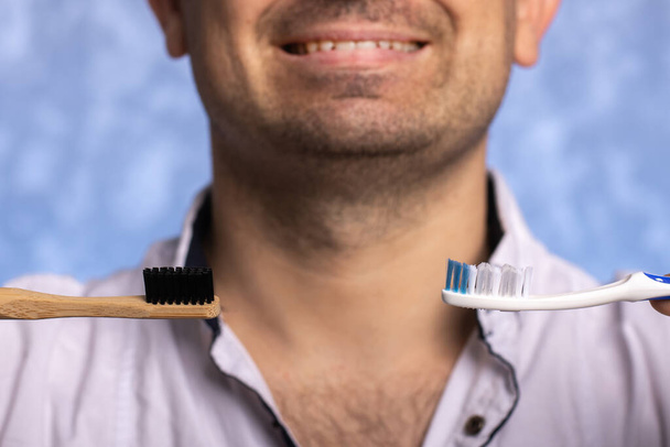 bambù biodegradabile e spazzolini di plastica in mano sullo sfondo di un uomo con un sorriso. eco concetto di scelta amichevole. prodotti per l'igiene
. - Foto, immagini