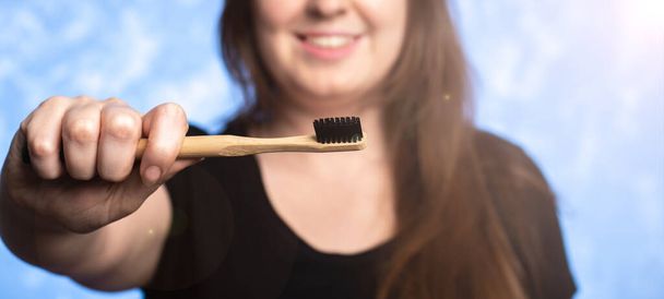 eco-friendly bamboo toothbrush in a female hand. girl with a snow-white smile on the background in defocus. oral hygiene. items from biodegradable materials. close-up. - Foto, immagini