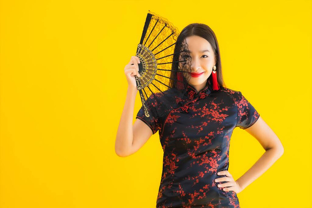 Πορτρέτο όμορφη νεαρή ασιατική γυναίκα φορούν κινέζικο φόρεμα με ανεμιστήρα για κινέζικο έννοια του νέου έτους σε κίτρινο απομονωμένο φόντο - Φωτογραφία, εικόνα