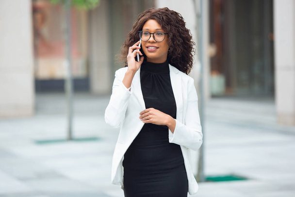 Красивая афро-американская хорошо одетая деловая женщина выглядит уверенно и занятой, успешной
 - Фото, изображение