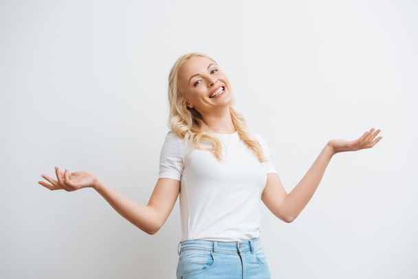 cheerful blonde woman smiling at camera while standing with open arms isolated on white - Photo, Image