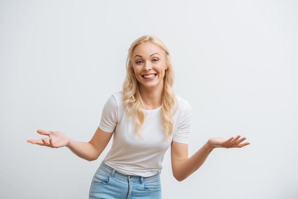happy blonde woman smiling at camera while standing with open arms isolated on white - 写真・画像