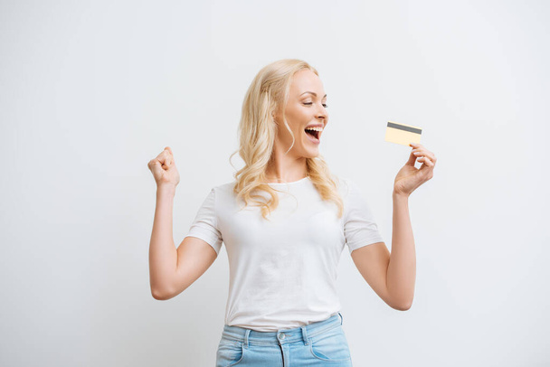 щаслива жінка, що показує жест переможця, тримаючи кредитну картку ізольовано на білому
 - Фото, зображення