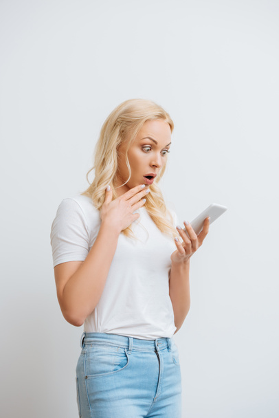шокированная девушка касаясь подбородок во время видеозвонка на смартфоне изолированы на белом
 - Фото, изображение