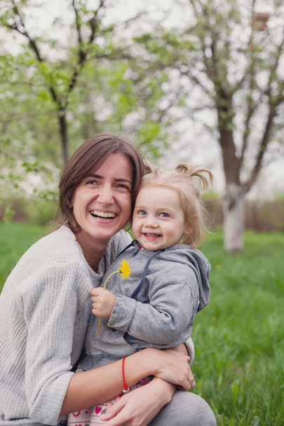 Portret van jonge moeder met twee jaar oude dochter in haar armen in de natuur.  - Foto, afbeelding