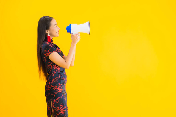 Portrait beautiful young asian woman wear chinese dress with megaphone on yellow isolated background - Photo, Image