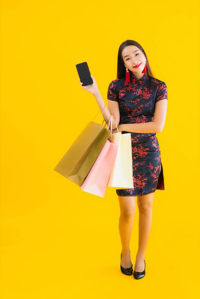 Portrait beautiful young asian woman wear chinese dress with shopping bag , smart mobile phone , credit card for chinese new year on yellow isolated background - Fotoğraf, Görsel