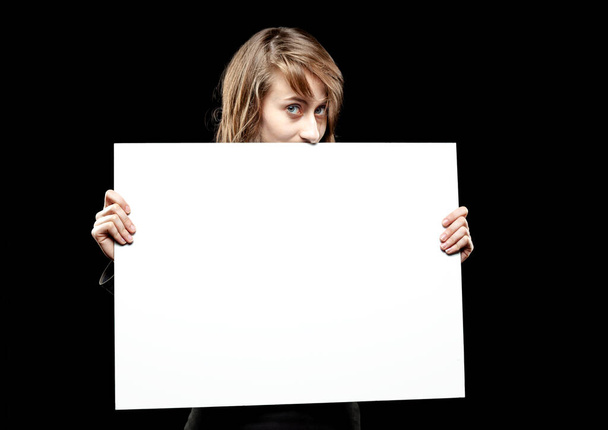 Teenage girl with an empty board for advertising and announcements. Fashion, portrait and people concept. Portrait of a young emotional woman on a dark background - Photo, Image