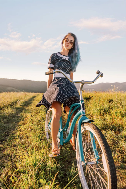 Mulher bonita em vestido sentado em um cruzador de bicicleta no caminho do campo em prados de verão
. - Foto, Imagem