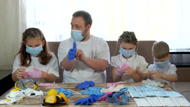 Papa laat kinderen met medische maskers zien hoe ze medische handschoenen aan moeten doen. Sociale afstand en zelfisolatie in quarantaine tijdens de COVID-19 pandemie. - Video