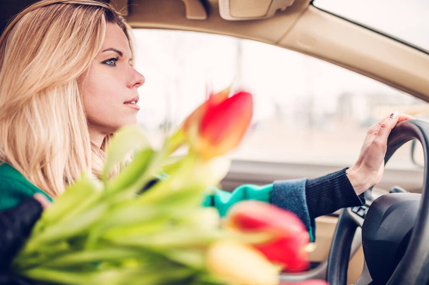 Beautiful attractive Scandinavian blonde returns from a date at the wheel of a car with a large bouquet of flowers - Foto, Imagem