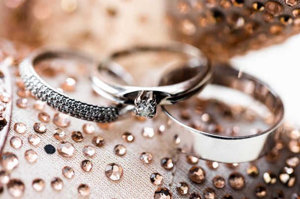 snubní prsteny, zlaté prsteny s drahými kameny pro nevěstu a ženicha zblízka na pozadí lesklých kamínků. Ghanský záblesk. - Fotografie, Obrázek