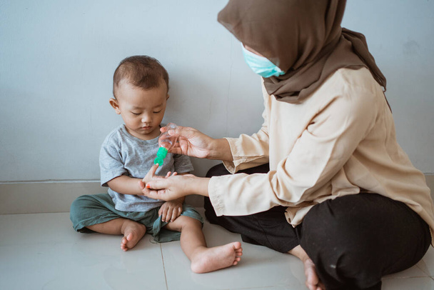muslim woman applying hand sanitizer to her son - Fotoğraf, Görsel