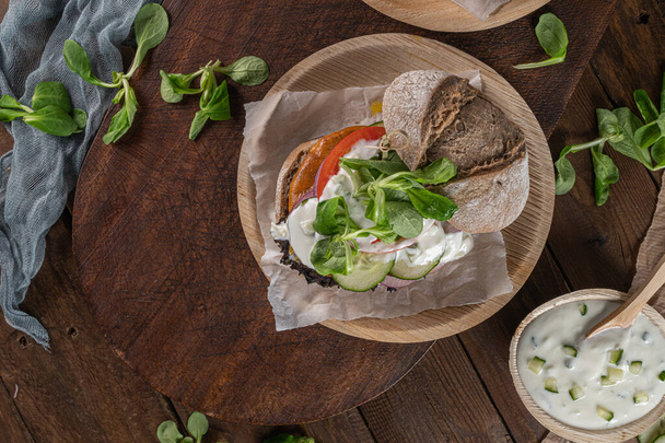 Healthy vegan burger with fresh vegetables and yogurt sauce on rustic kitchen counter top. - Fotografie, Obrázek