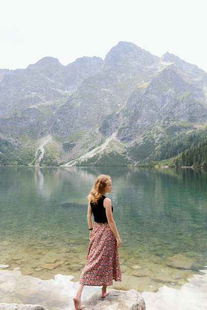 Lány egy elegáns szoknya a háttérben a tiszta tó és a magas hegyek. Lake Morskie Oko, Tátrai Nemzeti Park, Lengyelország - Fotó, kép