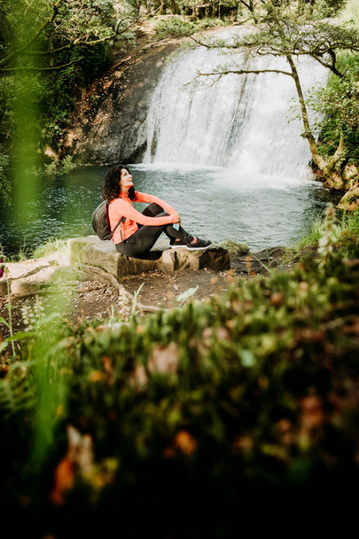 Γυναίκα κάθεται σε ένα βράχο μπροστά από έναν καταρράκτη - Φωτογραφία, εικόνα