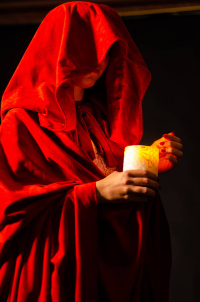 Όμορφη γυναίκα με κόκκινο μανδύα κρατώντας κερί. Δραματική και φανταστική σκοποβολή  - Φωτογραφία, εικόνα